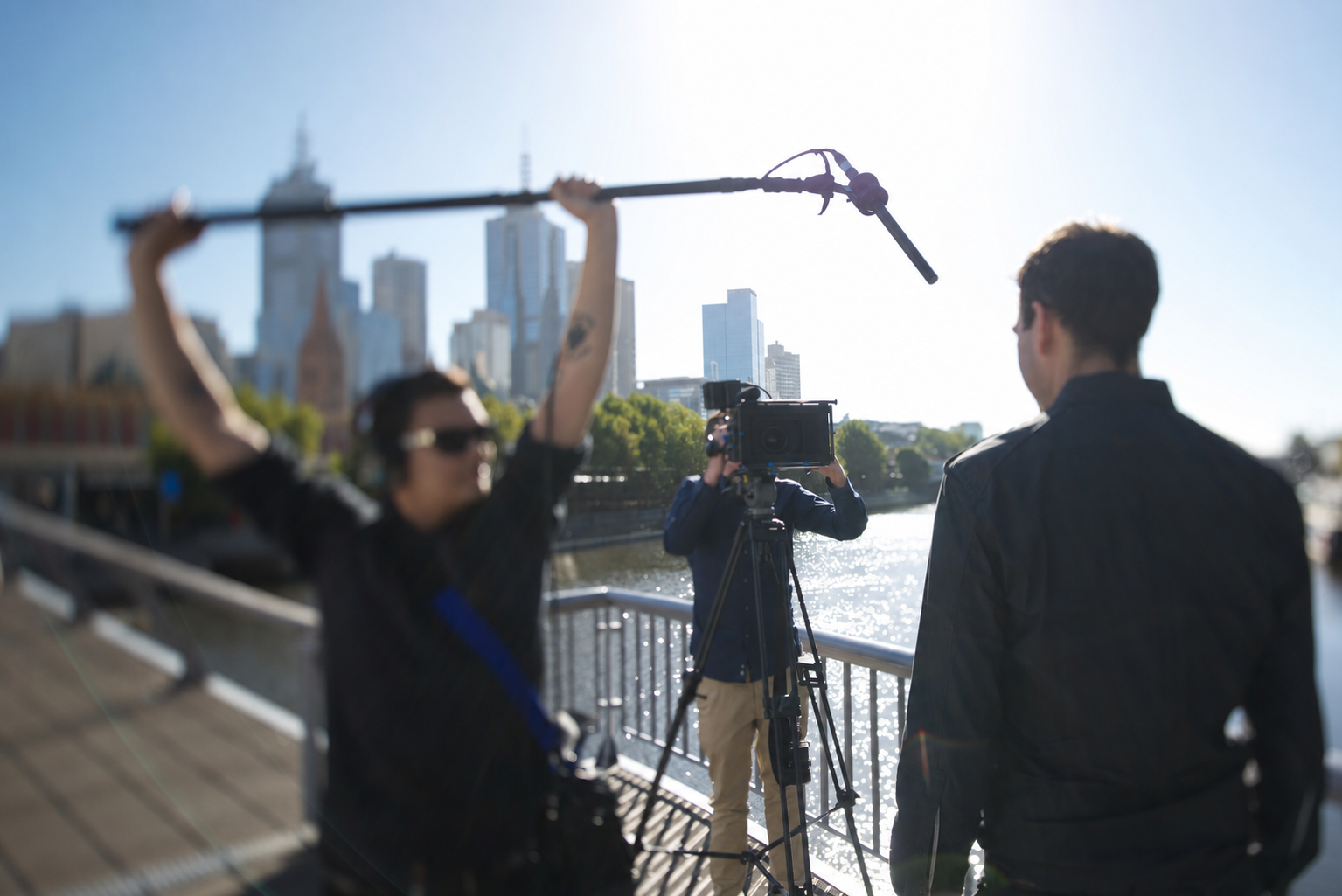 Melbourne camera crew filming beside the Yarra River with the city skyline behind them